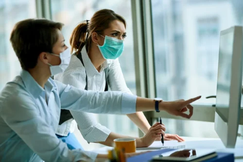 young-businesswoman-her-colleague-wearing-face-masks-while-working-computer-office-virus-epidemic
